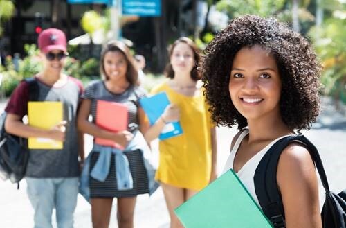 A girl holding a binder and a backpack smiling