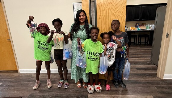 A woman and five kids stand and smile for a picture holding their art pieces.
