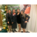 Barbara Huggins and 3 other women all stand together smiling in front of a banner. 