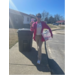 A woman walks down the street holding a bucket a stuffed bears.