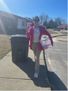 A woman walks down the street holding a bucket a stuffed bears.