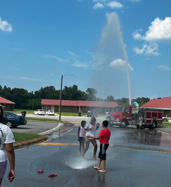 Children on a street playing in water from a fire truck.